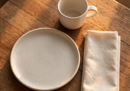 A single place setting at a small table in warm evening light, representing a full life held with contentment during a season of waiting.