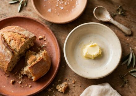 A simply set table with mismatched dishware and a loaf of bread, representing hospitality offered without a staged, perfect home.