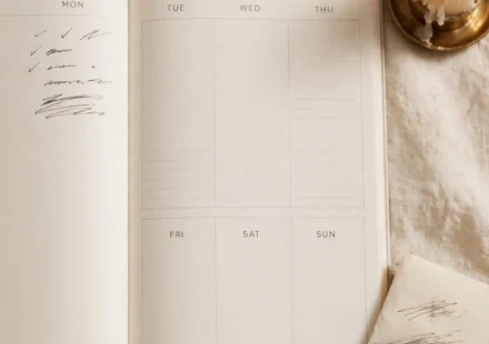 An open planner with only one day filled in beside a candle, representing planning one honest day at a time in an uncertain season.