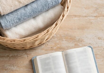 Folded laundry beside an open Bible on a kitchen table, representing the quiet spiritual weight of an ordinary day.