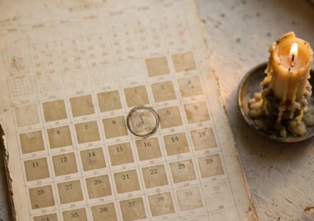 A wall calendar with a circled date long past, beside a candle in fading light, representing hope held through an unmoving timeline.