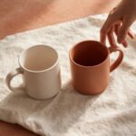 Two coffee mugs facing each other with a hand reaching toward one, representing a plain, honest apology softening a tense moment.
