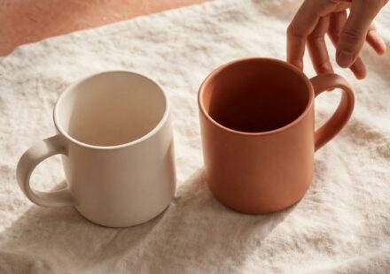 Two coffee mugs facing each other with a hand reaching toward one, representing a plain, honest apology softening a tense moment.