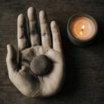A single stone resting in a bowl beside a candle, representing a burden held honestly rather than solved.