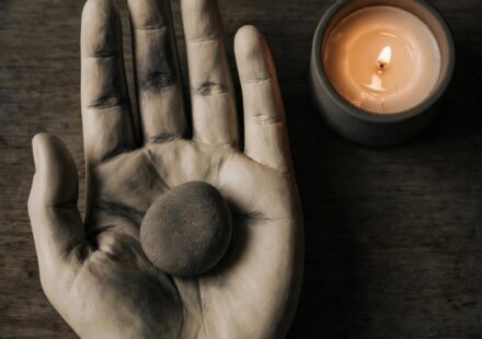 A single stone resting in a bowl beside a candle, representing a burden held honestly rather than solved.