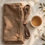 A folded work apron and a cup of tea rest on cream linen in soft late-afternoon light.
