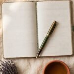 An open, blank planner lies on cream linen beside a terracotta mug of tea and a sprig of dried lavender in soft morning light.