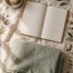 An open journal beside an unlit candle and a folded blanket, evoking a prayer left unfinished.