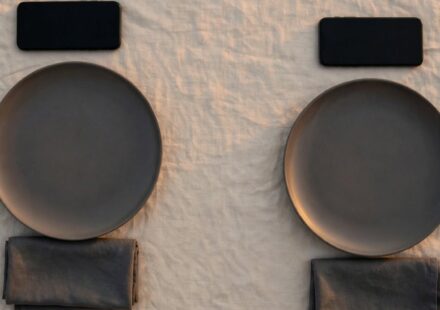 Two dinner plates set with a noticeable gap of empty table between them, representing quiet distance settling into a marriage.