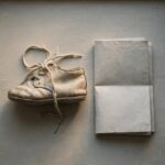 A worn baby shoe beside a folded letter on a windowsill, representing a parent's grief over a child who has walked away from faith.