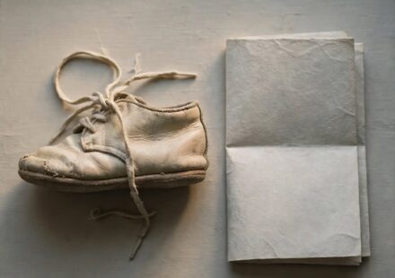 A worn baby shoe beside a folded letter on a windowsill, representing a parent's grief over a child who has walked away from faith.