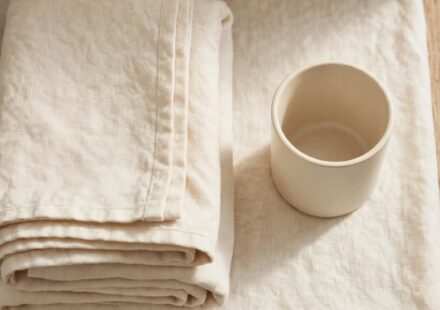 A folded guest towel and an empty cup sit on a shelf in soft natural light.