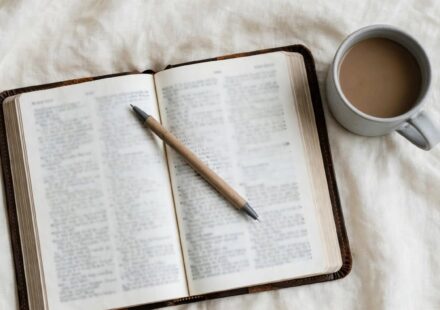 An open Bible and a lukewarm cup of coffee rest on cream linen in soft grey morning light.