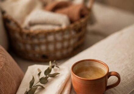 A cup of tea on the arm of a couch with a full laundry basket blurred behind it, representing rest taken before the list is finished.