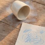 An overturned cup with a milk stain beside a child's drawing, representing a small moment repaired through a parent's honest apology.