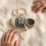 A child's untied shoe with two adult hands nearby, one holding back, representing two different but equally loving parenting instincts.
