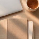 A folded sheet of paper tucked inside a closed book beside a closed laptop, representing worries written down and set aside for the weekend.