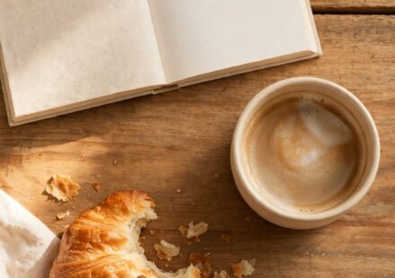 A slow weekend breakfast with coffee, a pastry, and an open book on a wooden table, representing enjoyment with no productive purpose attached.