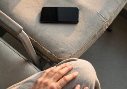 A phone face down on a waiting room chair beside a pair of open hands, representing letting go of control in the middle of a hard wait.