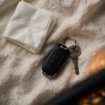 Car keys and a folded tissue rest on cream linen with a soft warm glow in the background.