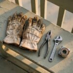 Worn work gloves set down on a porch railing beside untouched tools, representing a body forced to rest against its will.